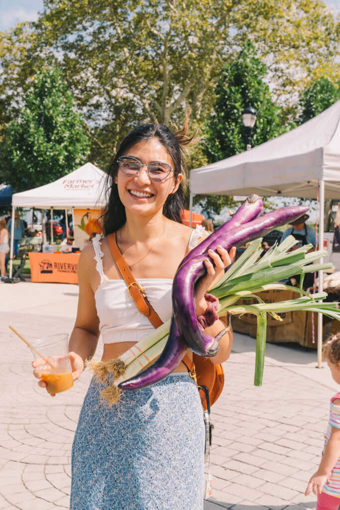 A female market patron poses with her leeks and Chinese eggplant.