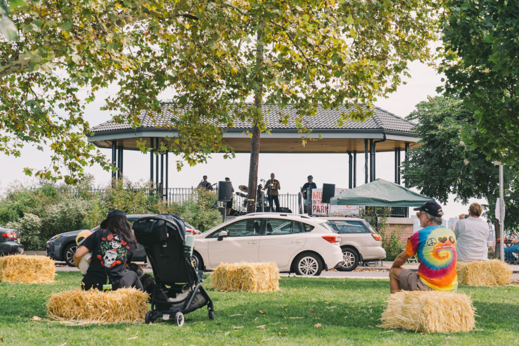 The Zydeco Revelators play in the distant gazebo while market patrons sit in the foreground on hay bales enjoying themselves.