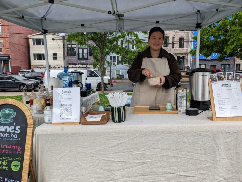 Photo of a woman at a farmers market booth selling green tea matcha drinks