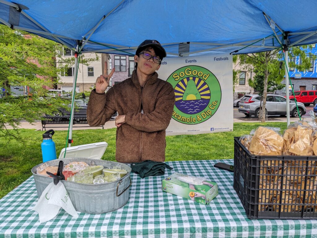 Photo of a young man at a farmers market booth selling guacamole