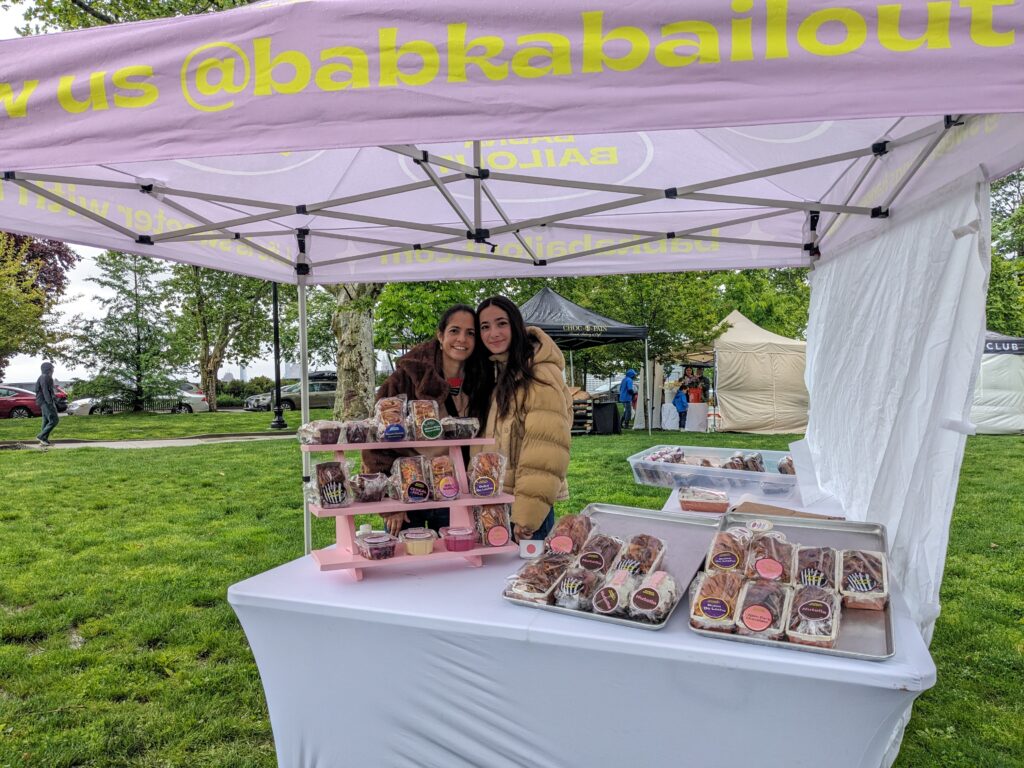 Photo of two women at a farmers market booth selling baked goods and dips