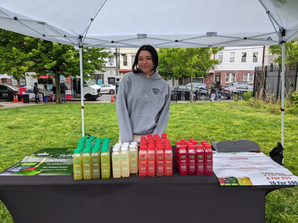 Photo of a woman at a farmers market booth selling fresh pressed juices