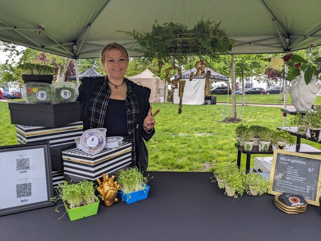 Photo of a woman at a farmers market booth selling microgreens