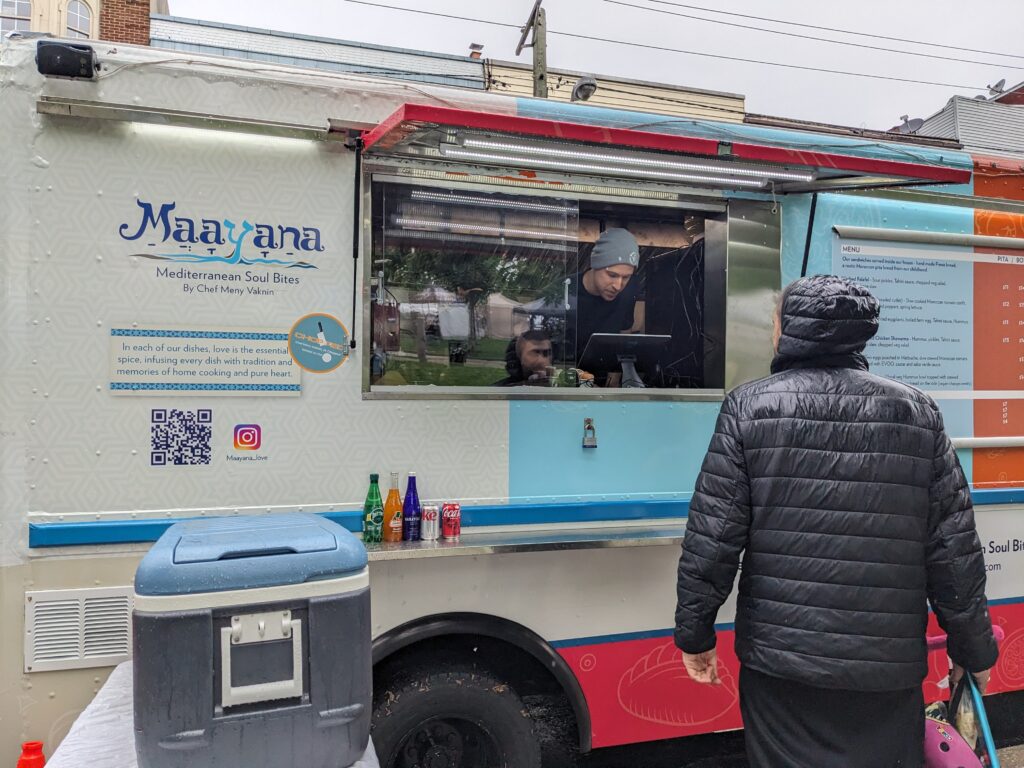 Photo of a customer ordering a meal at a beige & blue food truck at a farmers market selling middle eastern food