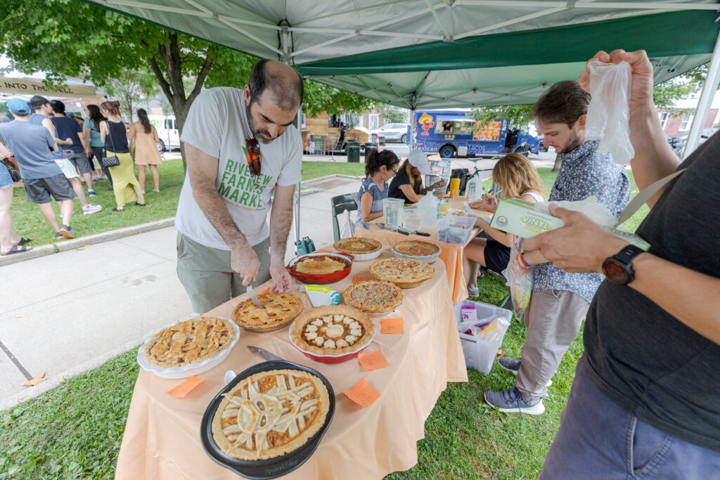 A spread of peach pies fill a table covered with a peach-colored table cloth.