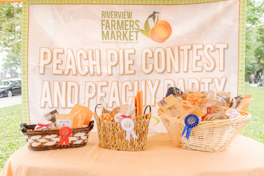 Three prize baskets sit on a table in front of a large banner that reads, Peach Pie Contest and Peachy Party