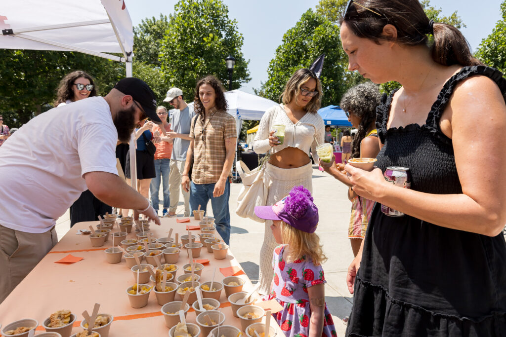 A volunteer hands out small cups filled with Peach Pie samples to a line of patrons.