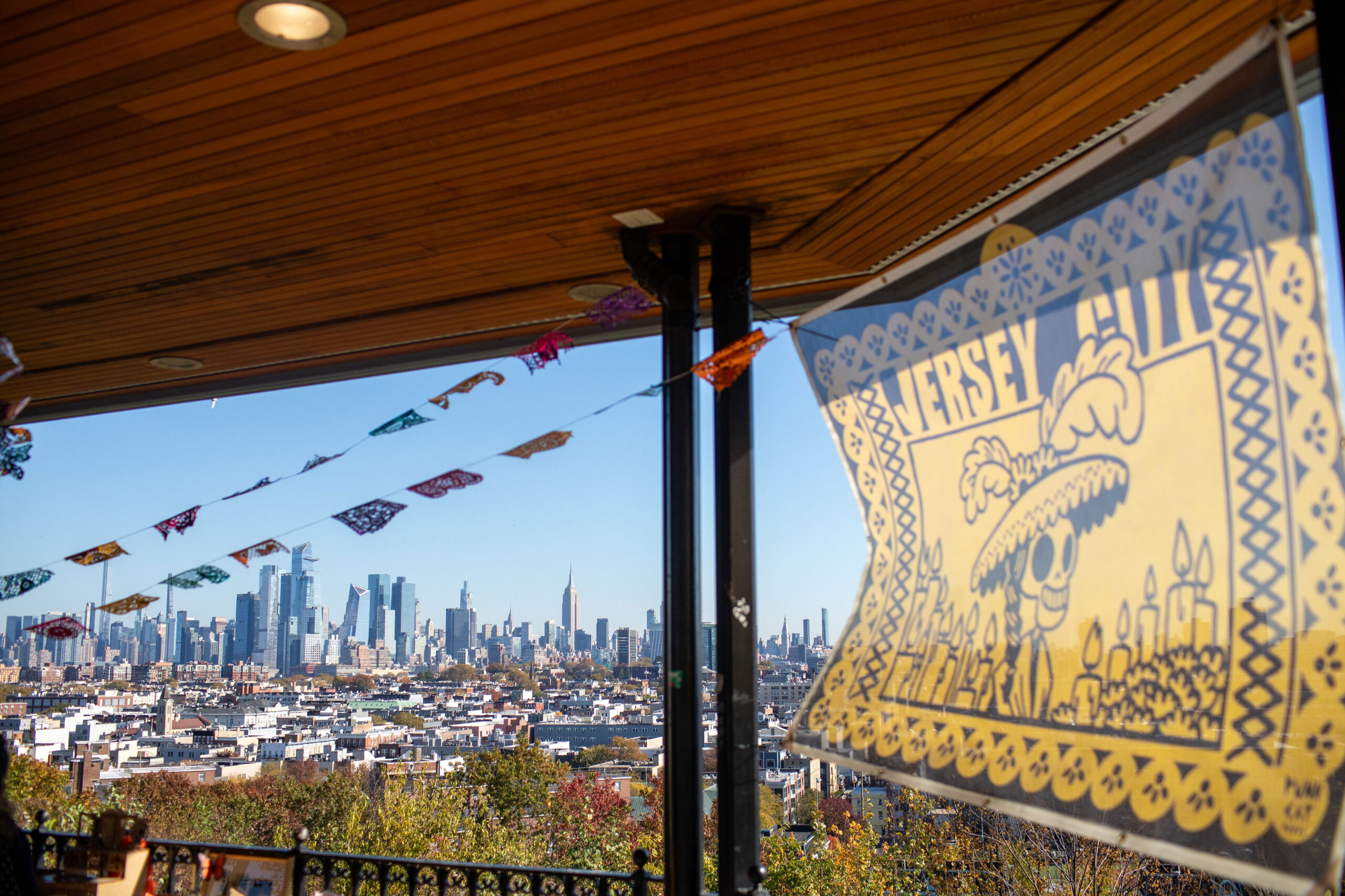 Day of the Dead banner and papel picado shown set up in a gazebo. In the background is the skyline of New York City.