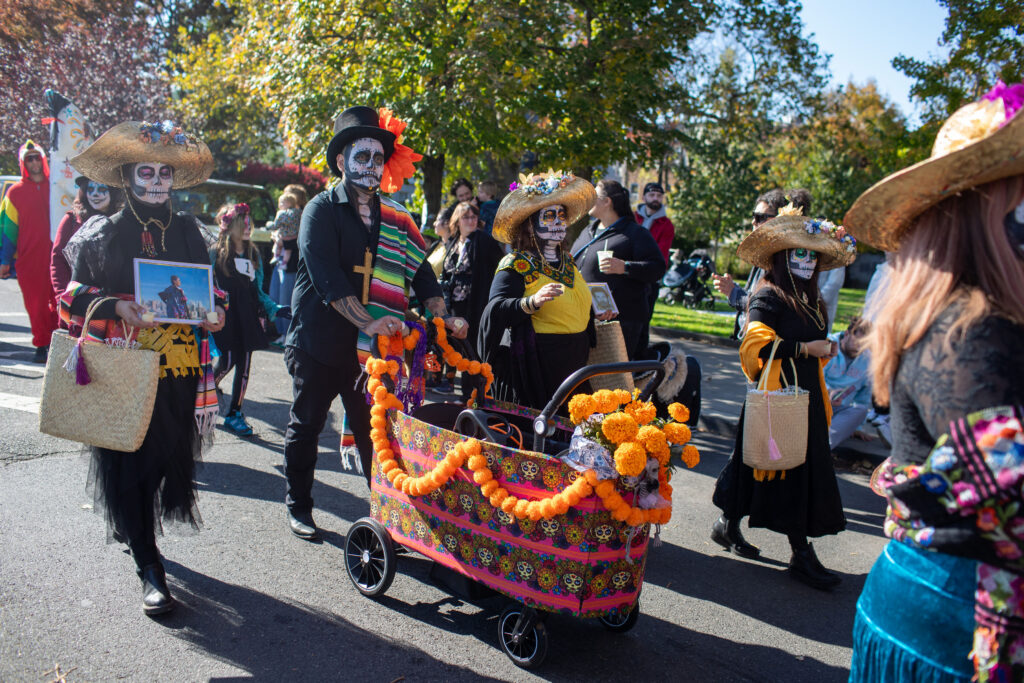 Families dressed up as La Catrina participating in the Day of the Dead parade. Colorful outfits with painted faces.